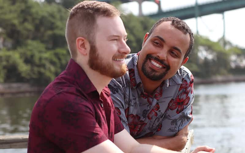 Two men outside by a river wearing shirts and smiling