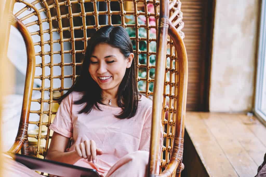 Woman in pink top sat on brown wicker chair looking down and smiling