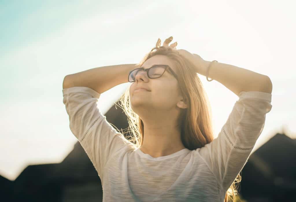Woman with her hands on her head wearing glasses with closed eyes and her hands on her head