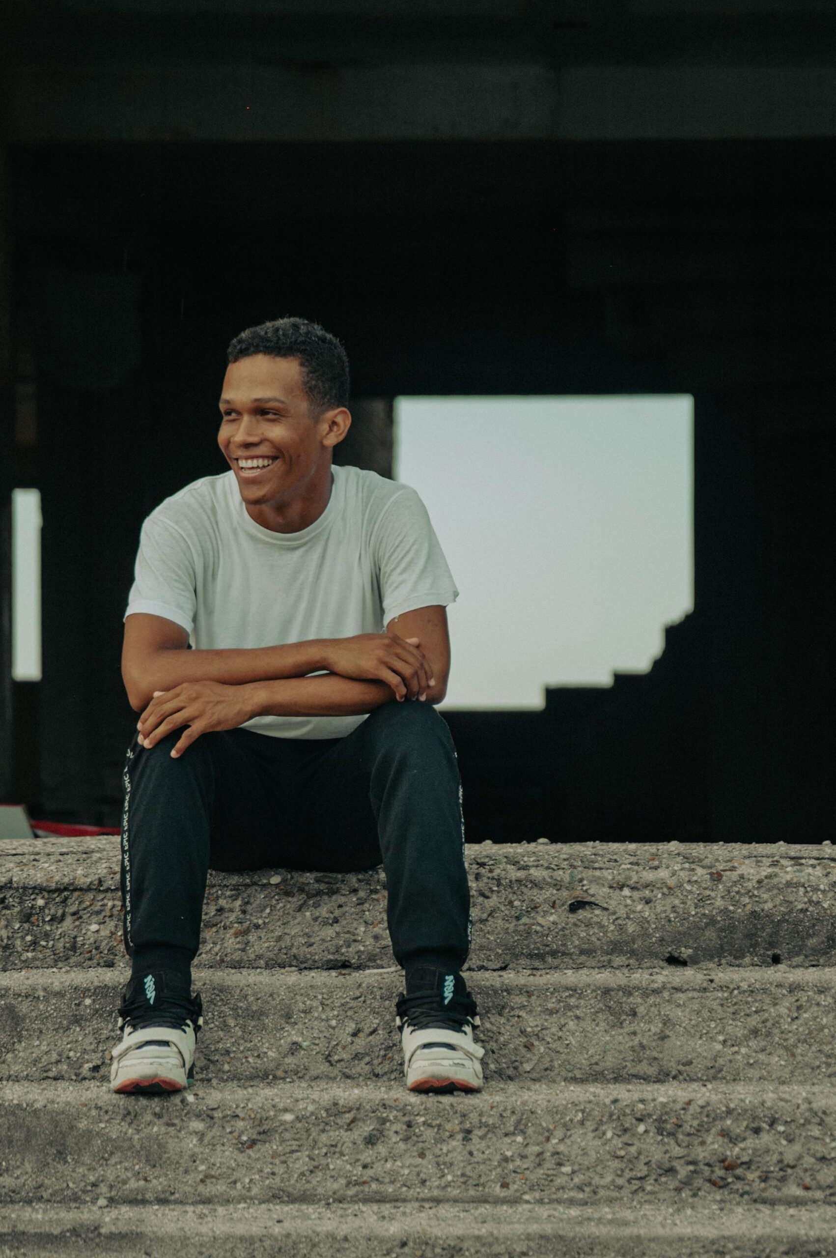 Man in casual wear sat on steps looking to his right and smiling.